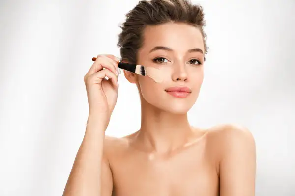 Donna applica fondotinta con pennello. Per un look naturale, il correttore deve essere più chiaro del fondotinta.